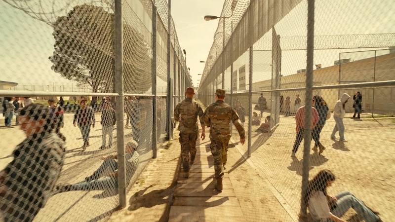 One Battle After Another, plano amplio con grupo de personajes en un exterior cercado, fotografía de Michael Bauman