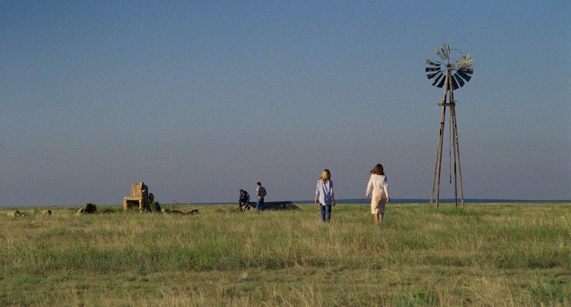 Plano general de la llanura en Badlands con dos figuras caminando y un molino al fondo, ejemplo del naturalismo visual de la película
