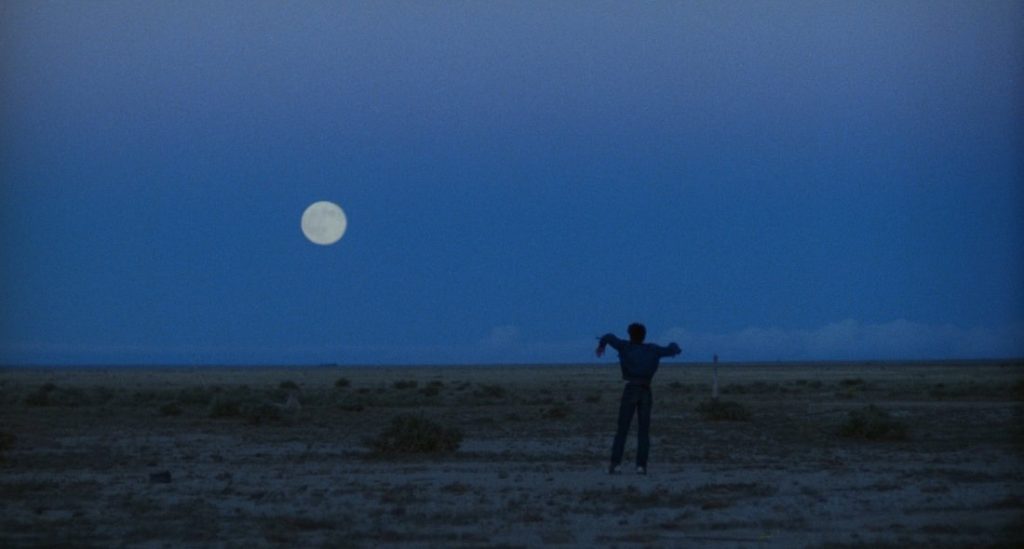 Figura solitaria bajo la luna en un paisaje nocturno azul de Badlands, imagen característica del lirismo visual de Terrence Malick
