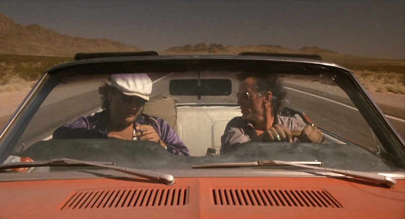 James Woods y James Belushi viajando en coche por un paisaje árido en Salvador, con fotografía cálida y naturalista de Robert Richardson